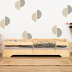 Lit en bois de couleur bois naturel avec des découpes dans les barrières latérales et équipé de barrières supplémentaires