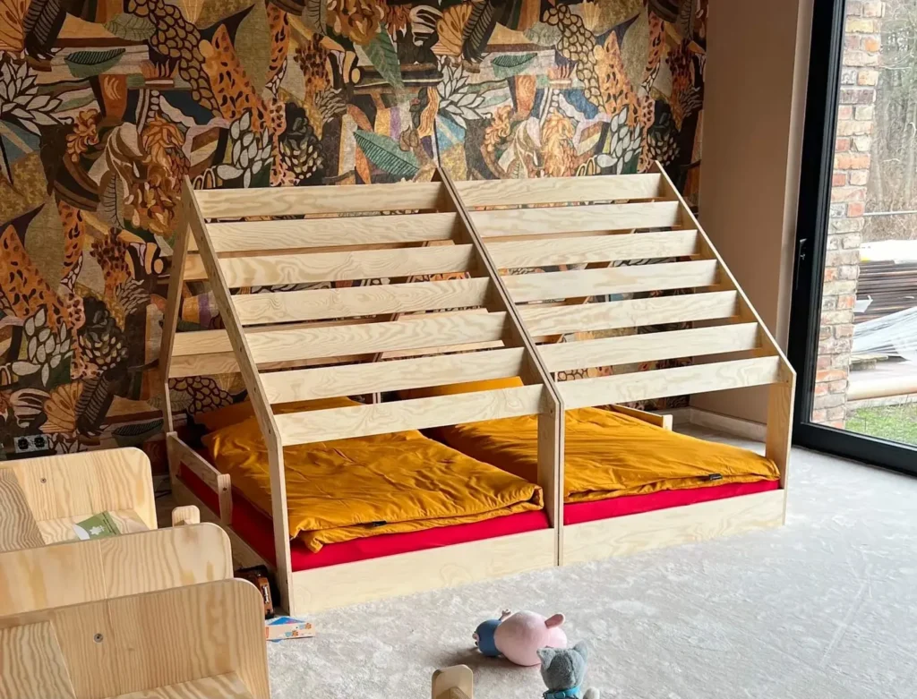 Deux lits d’enfants cabane en bois clair, placés côte à côte, avec une structure inclinée et une literie colorée.