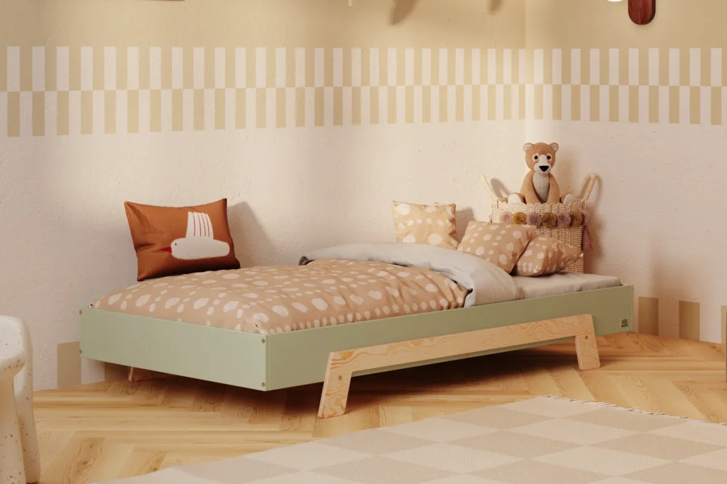 Lit enfant en contreplaqué de pin de couleur verte, avec des pieds en bois naturel, placé dans une chambre d’enfant chaleureuse avec un mur beige et une literie aux tons chauds.