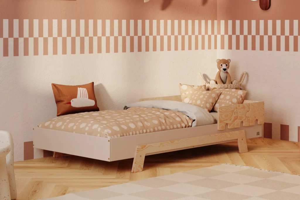 Lit enfant en contreplaqué de pin de couleur cachemire, avec une barrière en finition bois naturel et des pieds en bois naturel, placé dans une chambre d’enfant chaleureuse avec un mur beige et une literie aux tons chauds.