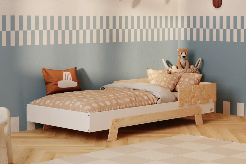 Lit enfant en contreplaqué de pin de couleur blanche, avec une barrière en finition bois naturel et des pieds en bois naturel, placé dans une chambre d’enfant chaleureuse avec un mur bleu et beige et une literie aux tons chauds.