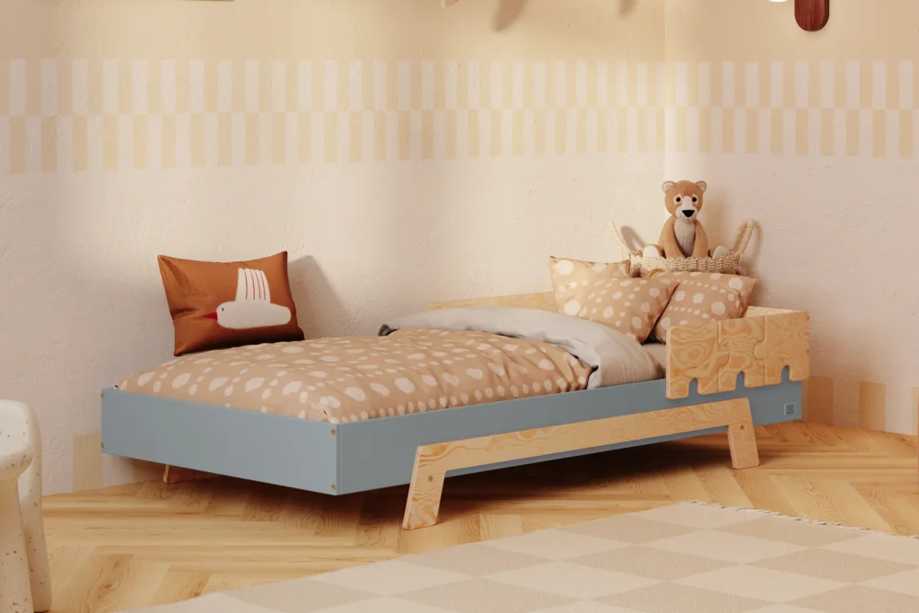 Lit enfant en contreplaqué de pin de couleur bleue, avec une barrière en finition bois naturel et des pieds en bois naturel, placé dans une chambre d’enfant chaleureuse avec un mur beige et une literie aux tons chauds.