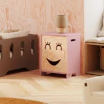 Armoire pour enfants en bois avec un visage souriant aux yeux fermés s’ouvrant vers la droite en couleur rose