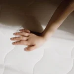 Main d’enfant touchant la surface douce et matelassée d’un matelas enfant blanc.