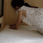 Fillette agenouillée sur un matelas enfant blanc installé sur un lit en bois.