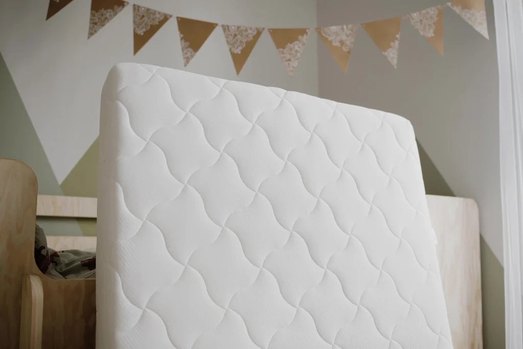 Matelas enfant blanc présenté à la verticale dans une chambre d’enfant.