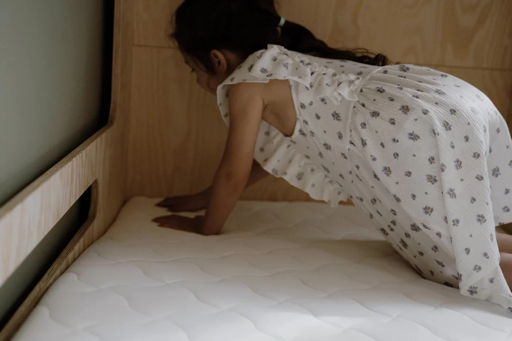 Fillette agenouillée sur un matelas enfant blanc installé sur un lit en bois.