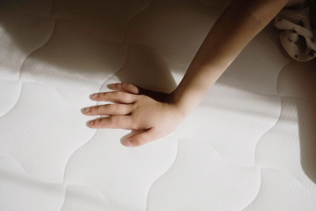 Main d’enfant touchant la surface douce et matelassée d’un matelas enfant blanc.