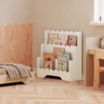 Bibliothèque Lulu blanche placée près de la fenêtre dans une chambre d'enfant, avec un lit et un bureau assortis cachemire. Espace lumineux et décor doux.