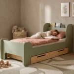 Chambre enfant avec un lit FLOU D vert avec tiroir et étagère intégrée – enfant dormant paisiblement dans un intérieur aux matériaux naturels