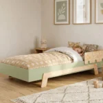 Lit enfant Smartwood PUZZLE BR1 en bois vert avec barrière dans une chambre lumineuse - petite fille endormie, toucher chaleureux et naturel du bois.