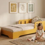 Lit enfant Smartwood TILA 6 en bois jaune avec barrières de sécurité dans une chambre lumineuse - petite fille jouant avec un arc-en-ciel Montessori à côté du lit, solution ergonomique favorisant une bonne posture et une colonne vertébrale saine.