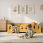 Chambre enfant avec un lit Montessori TILA 2 jaune avec barrière - petite fille jouant avec un doudou et des blocs en bois à côté de son lit sécurisé