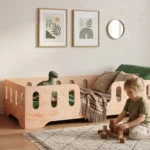 Lit enfant Smartwood TILA 2 en bois de pin avec barrières dans une chambre lumineuse - petite fille jouant avec des cubes en bois à côté du lit.