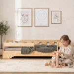 Chambre enfant avec un lit Montessori TILA 5S avec barrière en bois naturel – petite fille construisant une tour de blocs à côté de son lit sécurisé en contreplaqué de pin