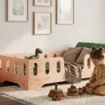 Lit enfant Smartwood TILA 2 en bois naturel avec barrières — petite fille jouant avec des cubes en bois à côté du lit.