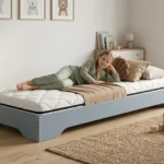 Lit enfant Smartwood TILA 7 en bois bleu avec matelas Smart Comfort - petite fille souriante allongée sur le lit dans une chambre lumineuse.