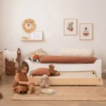 Lit enfant TILA 10 blanc en bois avec tiroir formant un couchage d'appoint, fillette jouant avec des cubes en bois dans une chambre cocooning.