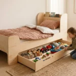 Lit enfant FLOU D en bois naturel avec tiroir coulissant, garçon sortant des affaires du tiroir dans une chambre lumineuse.