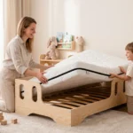Lit enfant TILA 1 en bois naturel avec matelas, maman et fils installant le matelas sur le sommier dans une chambre lumineuse.