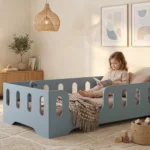 Lit enfant Montessori TILA 2 bleu avec barrières ajourées, une fillette assise sur le lit lisant un livre.