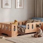 Lit enfant TILA 2 en bois naturel avec barrières ajourées, un garçon joue avec une petite voiture en bois près du lit.