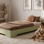 Lit enfant TILA 7 vert sauge, conception basse au sol, une fillette construit une tour de cubes près du lit.