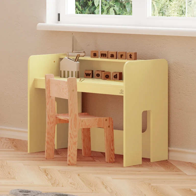 Bureau MIMI couleur beurre installé sous une fenêtre, avec une chaise en bois naturel et des accessoires éducatifs.