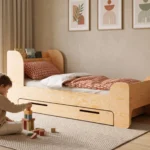 Lit enfant FLOU D en bois naturel avec tiroir de rangement, petit garçon jouant aux cubes sur le tapis à côté du lit.