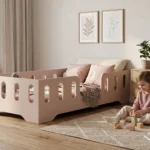 Lit enfant TILA 2 cachemire avec barrière et découpes ovales, petite fille jouant aux cubes sur le tapis à côté du lit.
