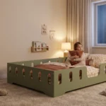 Lit enfant TILA 2 XL vert avec barrières sur tout le pourtour, petite fille assise dans le lit serrant un coussin, veilleuse allumée.