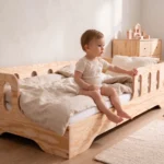 Lit enfant TILA 1 coloris naturel avec barrières ajourées, tout-petit assis au bord du lit dans une chambre lumineuse.