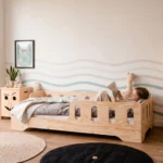 Lit enfant TILA 1 coloris naturel avec barrières ajourées, petite fille allongée qui lit un livre avec sa peluche.