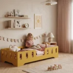 Lit enfant TILA 2 coloris moutarde avec barrières ajourées, petite fille assise sur son lit qui lit un livre avec ses peluches.