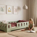 Lit enfant TILA 2 coloris vert avec barrières ajourées, petite fille assise sur le tapis qui feuillette un livre à côté du lit.