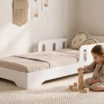 Lit enfant TILA 6 blanc avec barrière ajourée et entrée basse, petite fille qui empile des cubes en bois sur le tapis.