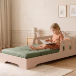 Lit enfant TILA 6 coloris cachemire avec barrières ajourées, petite fille assise qui lit un livre sur son lit.