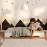Lit enfant TILA 7 blanc, bas et sans barrières, petite fille assise qui lit un livre devant un mur aux montagnes peintes.