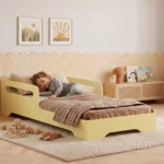Lit enfant TILA 3 coloris beurre avec barrière sur un côté, petit garçon endormi sous une couette beige dans une chambre lumineuse.